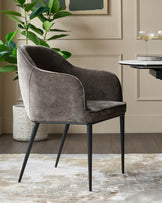 A brown velvet dining chair with armrests and black legs, placed on a patterned rug in a modern dining room.