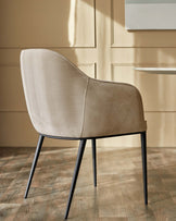 A modern beige chair with black metal legs sits on a wooden floor against a beige panelled wall.
