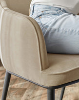 Beige upholstered chair with grey metal frame, someone wearing jeans is sitting on it.