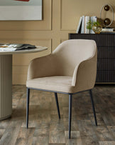 Stylish beige upholstered dining chair with black metal legs, placed next to a round dining table.
