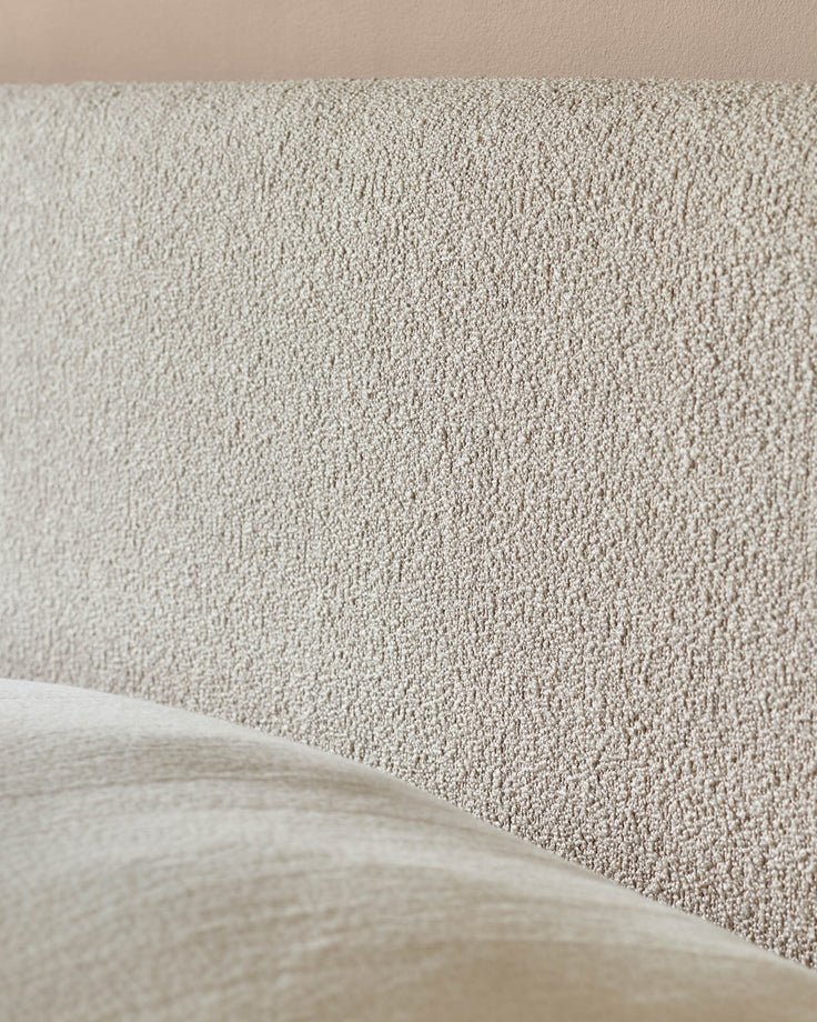 Close-up of a neutral-toned, textured headboard and a portion of the upholstered bed frame. Modern bedroom furniture.