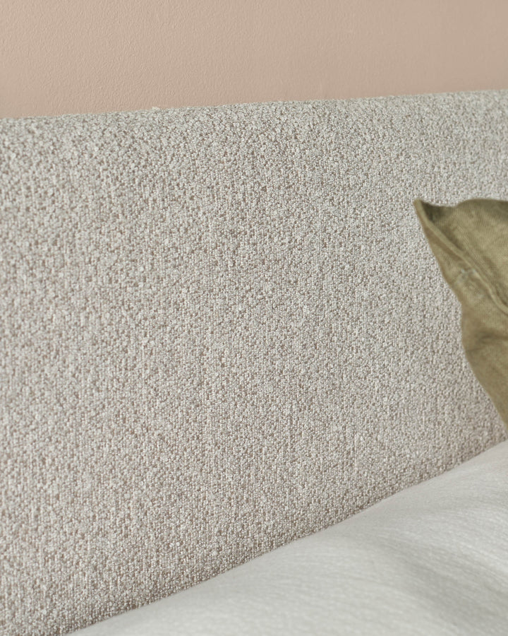 Close-up of a textured headboard with a neutral colour palette, featuring a soft pillow and white bedding.