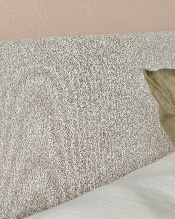 Close-up of a textured headboard with a neutral colour palette, featuring a soft pillow and white bedding.
