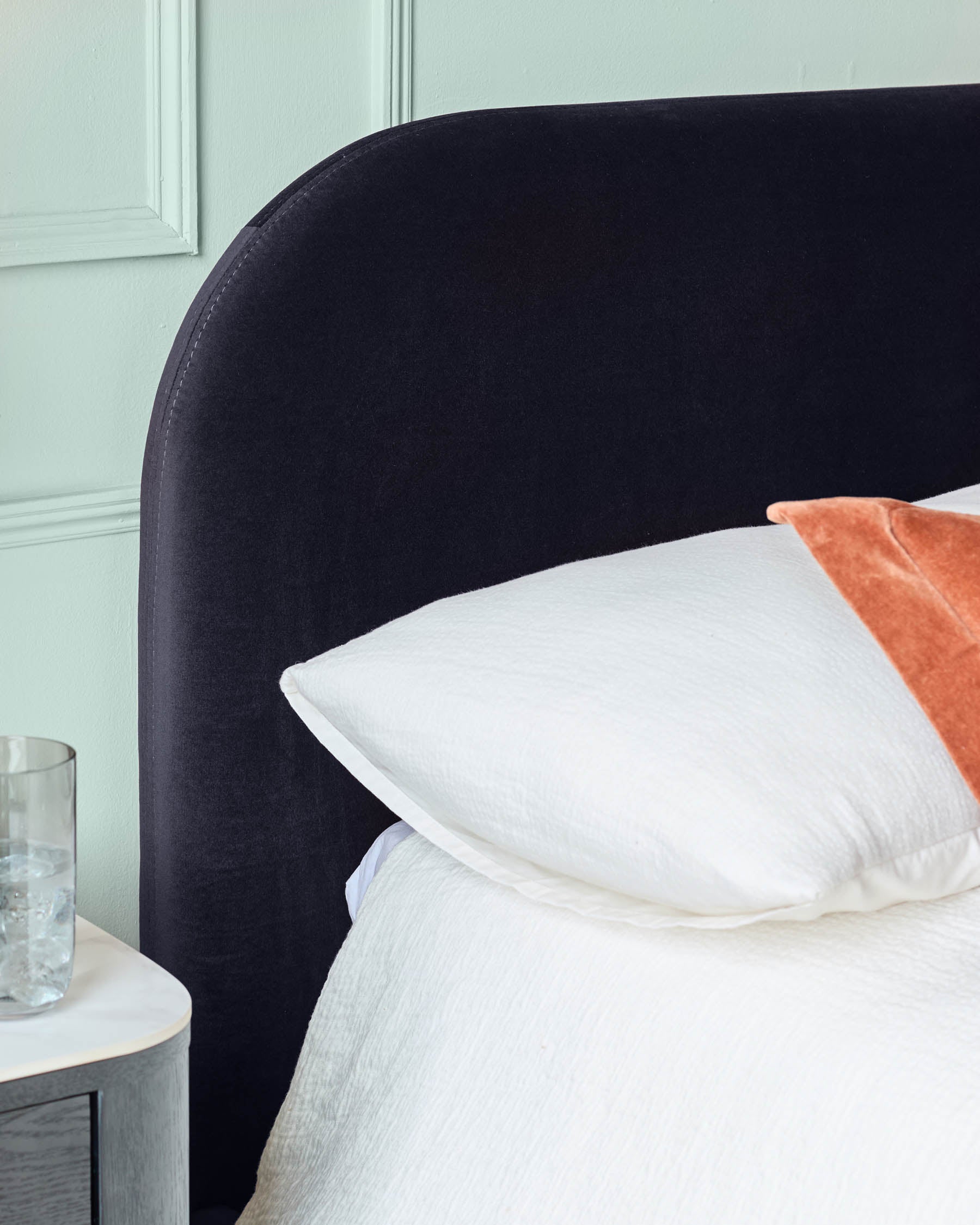 A stylish bedroom featuring a dark headboard, white textured bedding, and a modern bedside table.