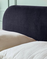 Close-up of a bed with a stylish, curved, dark headboard and soft, textured bedding and pillows.