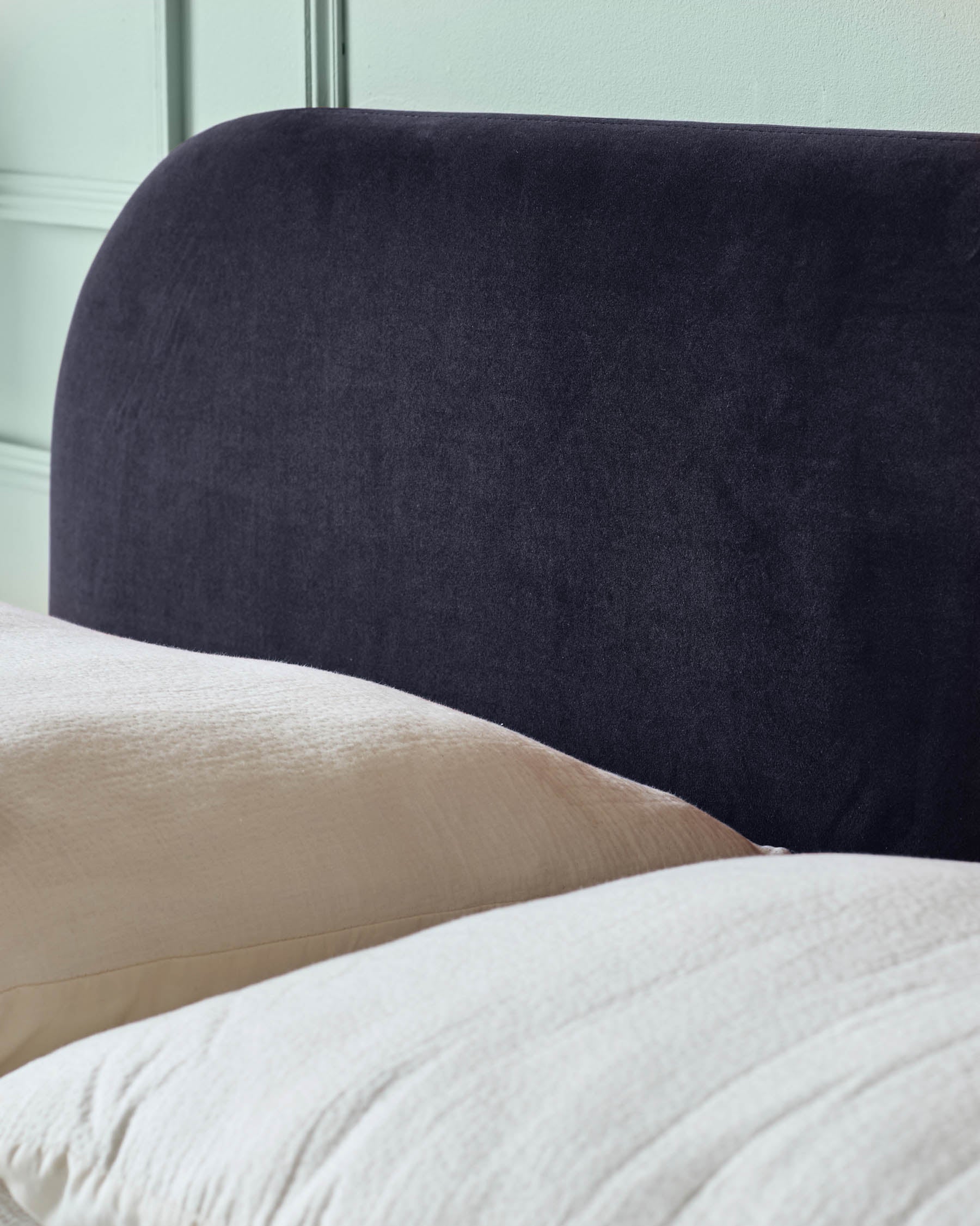 Close-up of a bed with a stylish, curved, dark headboard and soft, textured bedding and pillows.