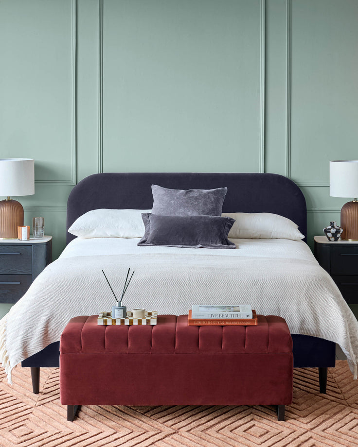 Bedroom featuring a plush bed, bedside tables with lamps, and a stylish ottoman, all complemented by a textured rug.