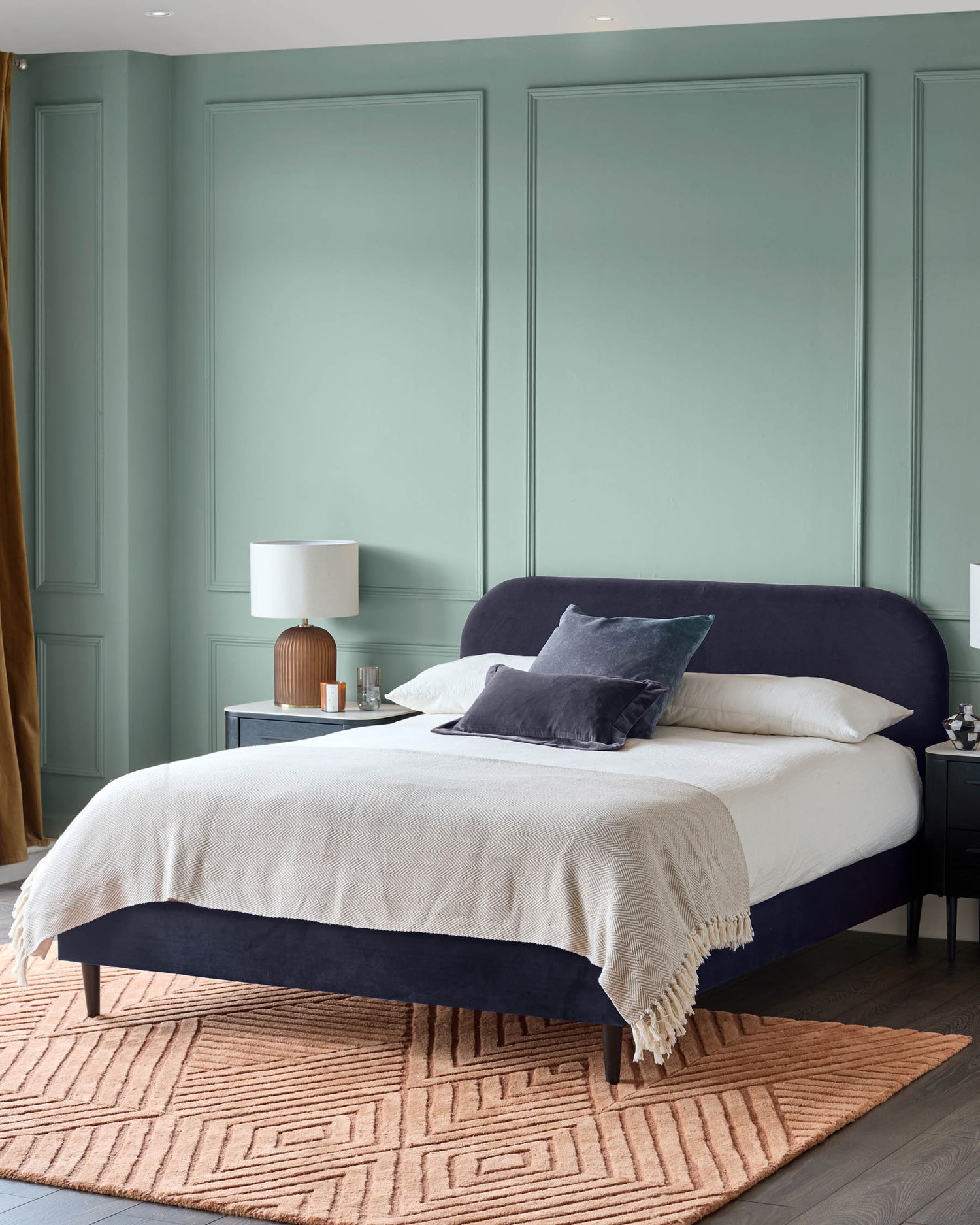 A bedroom with a plush, dark blue bed, white linen, side tables, and a patterned rug. A calming and stylish space.