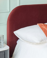 A stylish bedroom featuring a plush maroon headboard, crisp white bedding, and a chic bedside table with a glass of water.