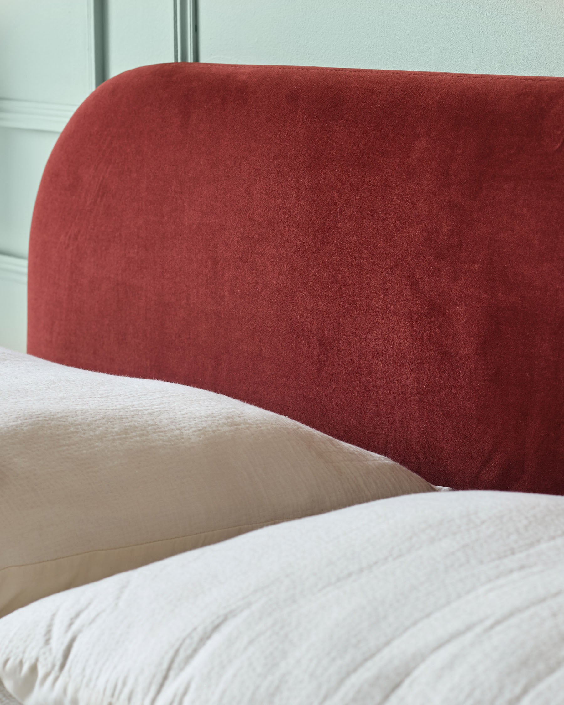 A close up of a bed with a red headboard and cream pillows and duvet. The headboard is rounded at the top.