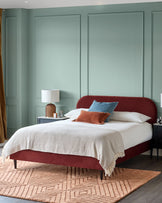 Bedroom featuring a red upholstered bed with a patterned rug, bedside tables with lamps, and light green panelling.