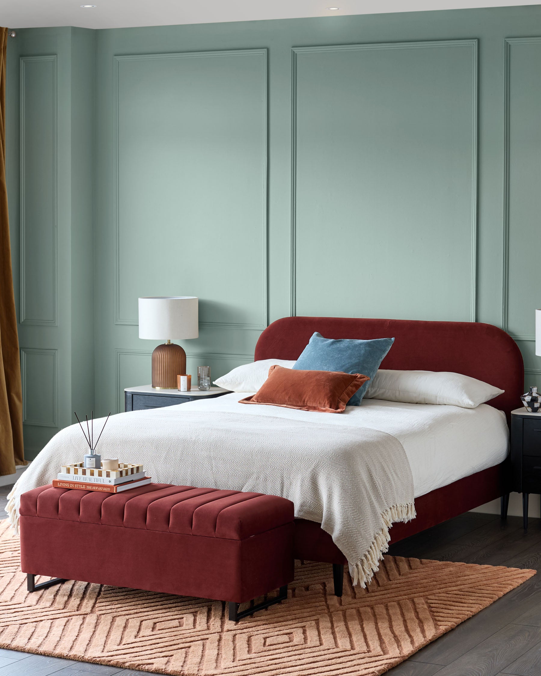 A bedroom with a red bed, ottoman and rug. There are two bedside tables and lamps on either side of the bed.