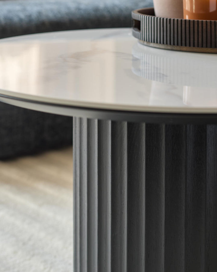 Close-up of a stylish round coffee table with a white marble top and a dark, fluted wooden base.