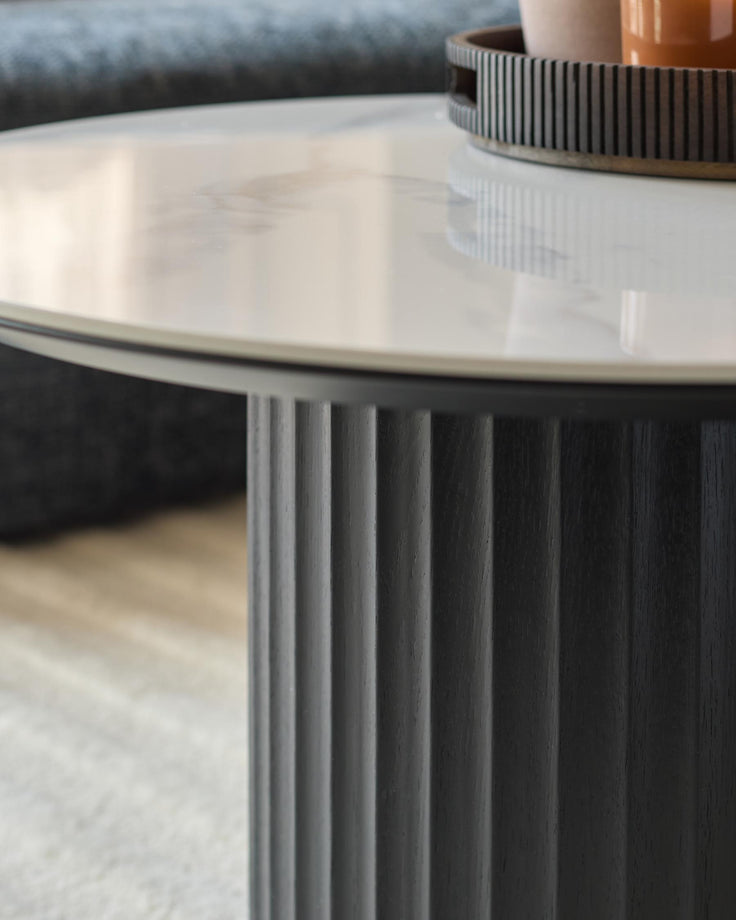 Close-up of a stylish round coffee table with a white marble top and a dark, fluted wooden base.