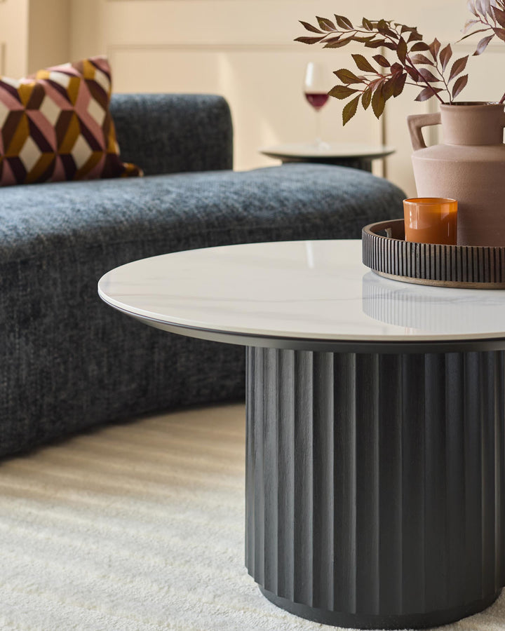 Close up of a modern living room with a round marble coffee table, a grey sofa and a geometric patterned cushion.