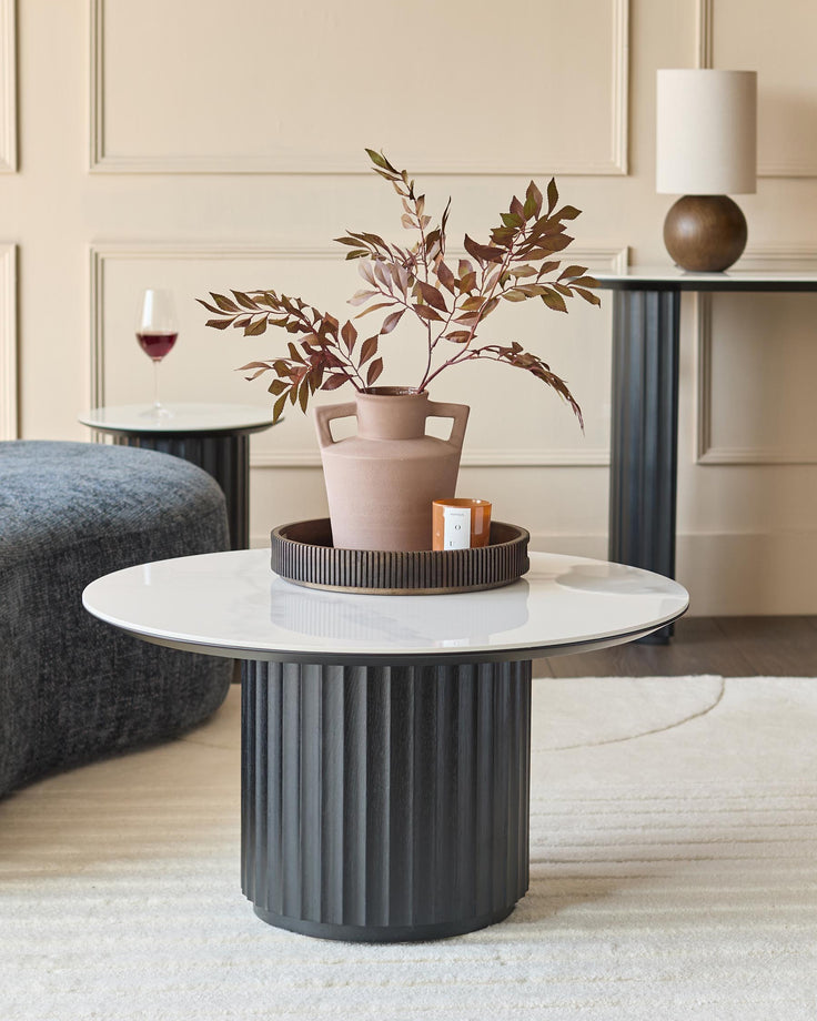 Stylish living room furniture: A round coffee table with marble top, a lamp table and a grey pouffe on a cream rug.