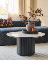 A modern living room featuring a stylish grey sofa, a patterned cushion and a round coffee table with a floral arrangement.