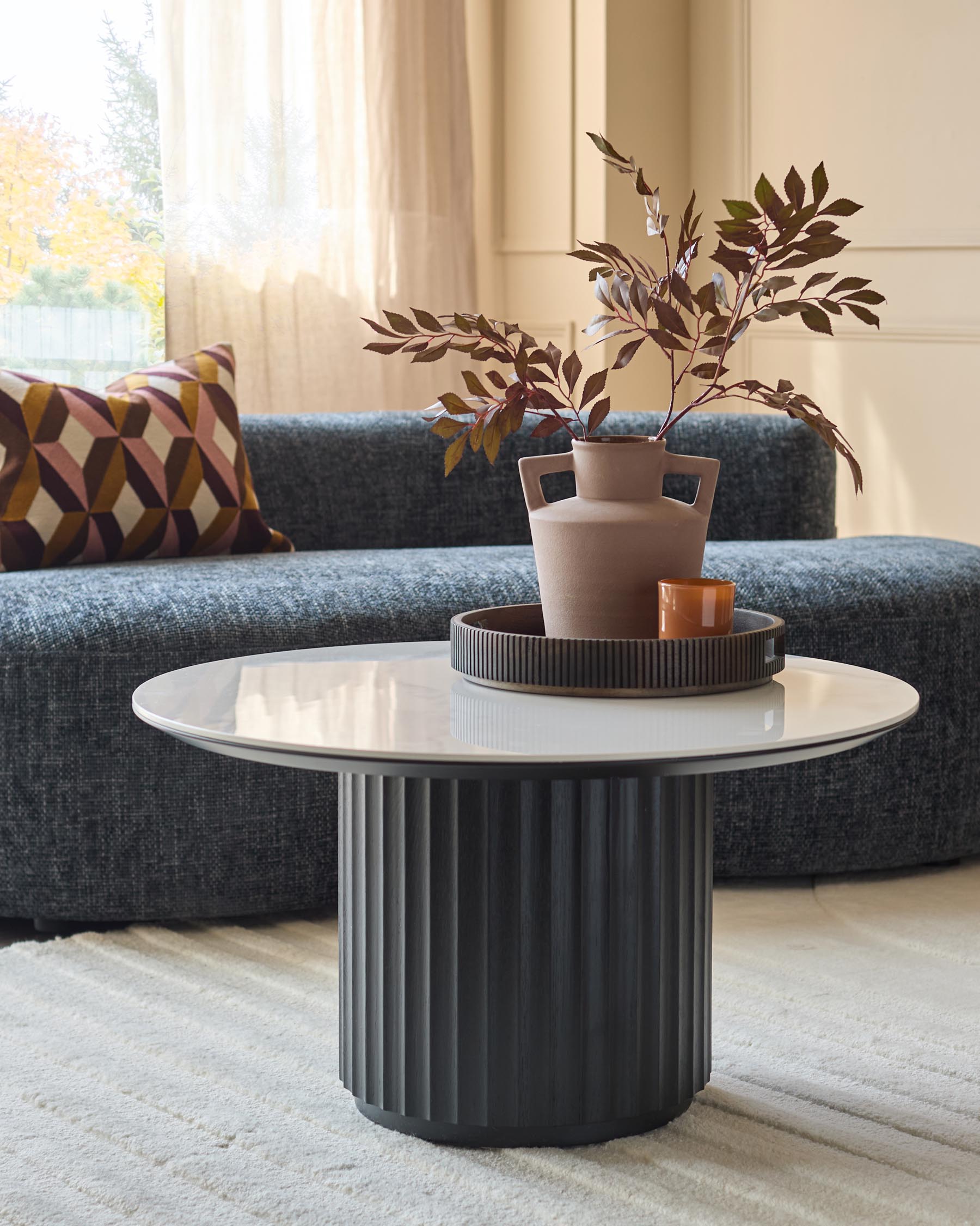 A modern living room featuring a stylish grey sofa, a patterned cushion and a round coffee table with a floral arrangement.