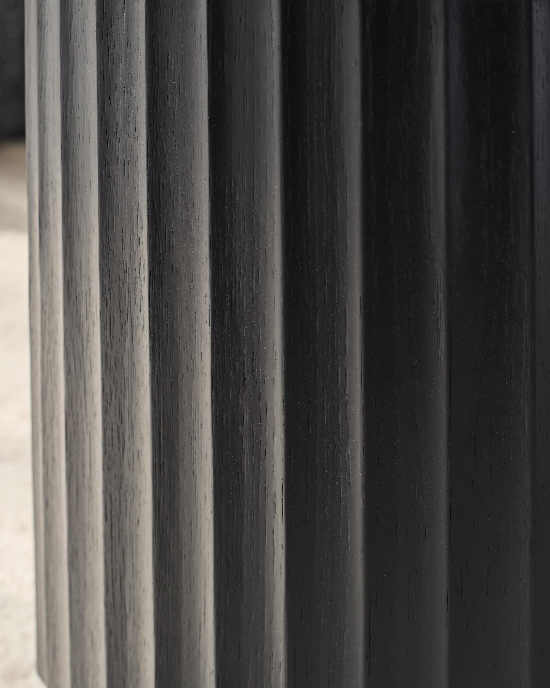 Close-up of a fluted black wooden furniture leg. Strong vertical lines and textured finish.