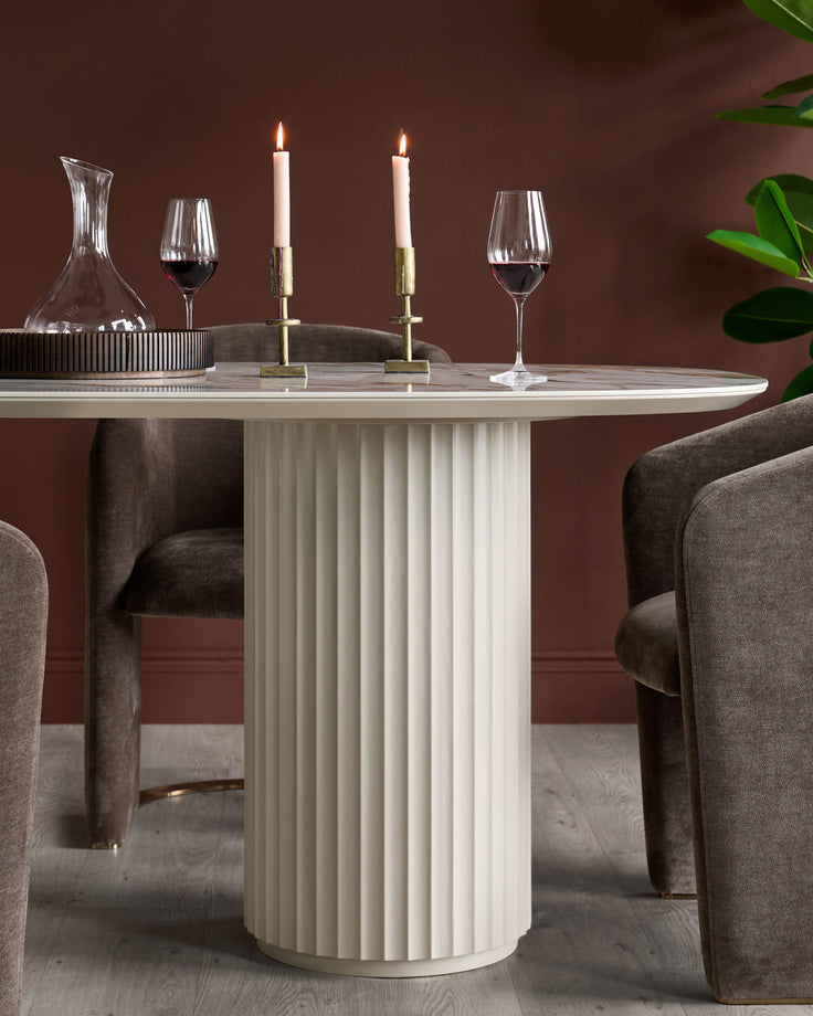 A round, cream table with a fluted base and brown velvet chairs, complete with wine glasses and candles.