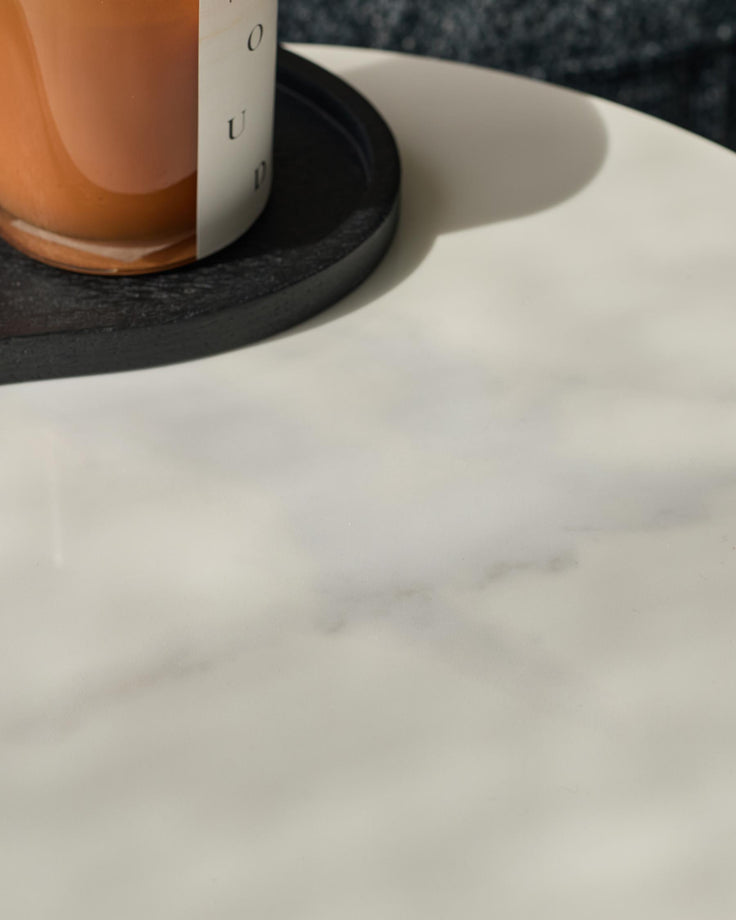 A candle and black tray sit atop a white marble table. The sleek design adds a touch of modern elegance to any room.