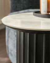 A round side table with a marble top and a black, fluted base, offering a sleek and modern design for any living space.