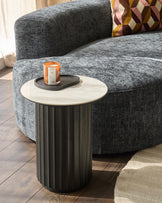 A grey sofa with a decorative cushion next to a round side table with a candle.