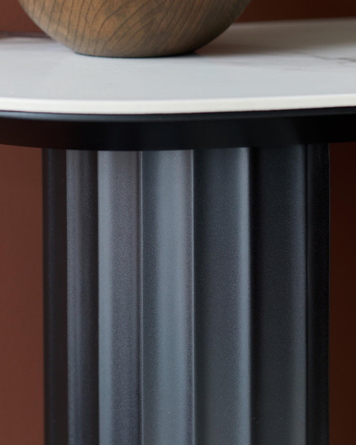 Close-up of a modern table with a fluted black base and a white top. A wooden bowl is on the table.