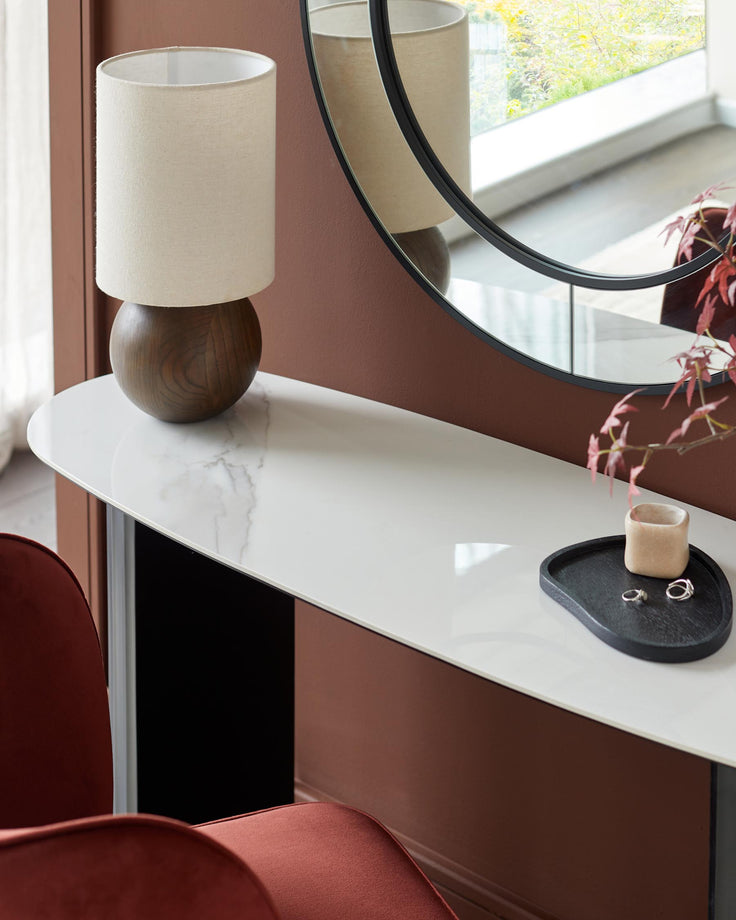 Marble-topped console table with round mirror above, complemented by a stylish lamp and accessories. Part of red chair visible.