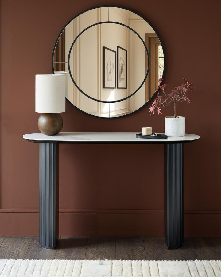 A stylish console table with a marble top, fluted legs, and a round mirror. It's a modern design for an entryway or living room.
