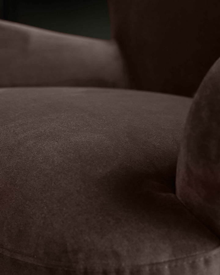 Close-up of a brown, plush velvet armchair. Focus is on the soft, textured seat and armrest.