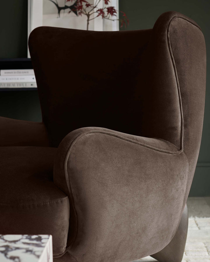 Close-up of a luxurious brown velvet armchair with curved armrests and high back, exuding comfort and sophistication.