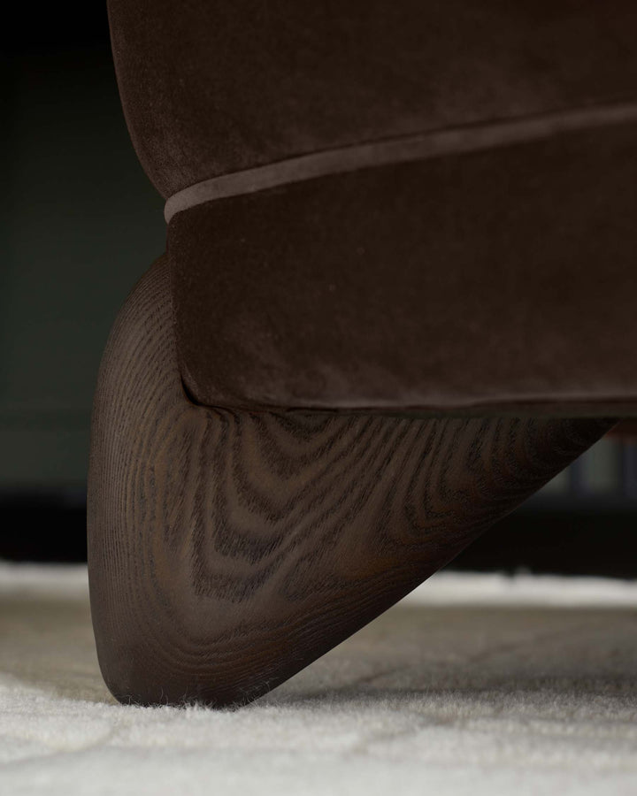 Close-up of a brown velvet sofa with a dark wood leg, resting on a cream-coloured rug.
