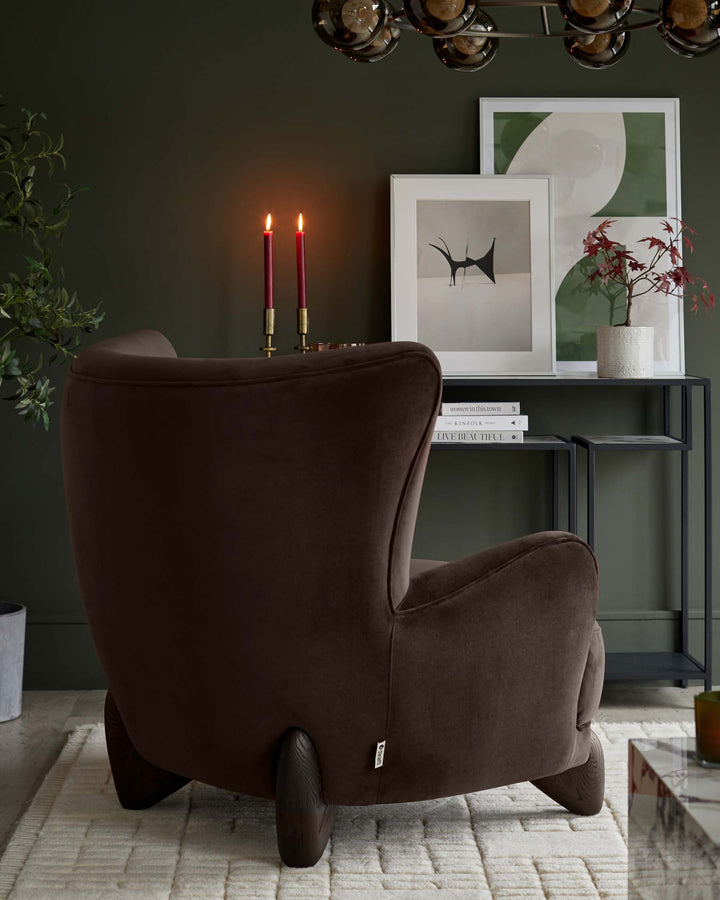 A brown velvet armchair sits on a cream rug in a warmly lit room with a side table.