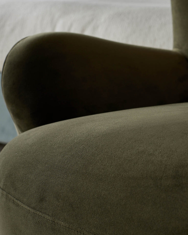 Close-up of a stylish olive green velvet armchair. The textured fabric and curved armrest suggest comfort and modern design.