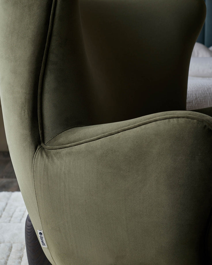 Close-up of an olive green wingback chair with dark wooden legs and a textured fabric finish.