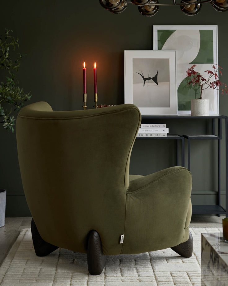 Olive green armchair with dark wooden legs, with a black shelving unit and assorted decorations behind it.