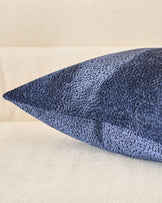 Navy blue textured cushion with pointed ends, displayed at an angle against a cream background.