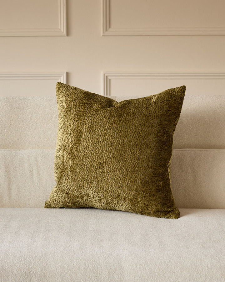 Harlene cushion in medium olive green, square shape with textured woven fabric, displayed on a cream sofa.