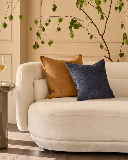 Navy textured cushion displayed on a cream armchair in a styled living room setting.