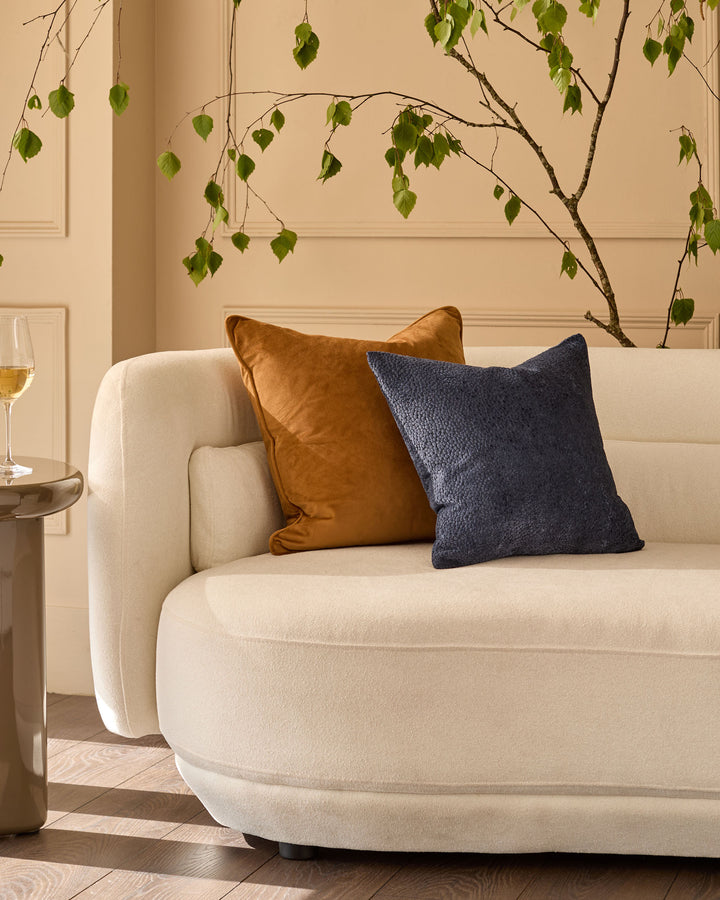 Large caramel cushion on cream armchair, styled with navy pillow in modern living room setting.