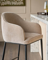 Harley bar stool in champagne fabric with curved backrest and black metal legs, positioned at marble counter.