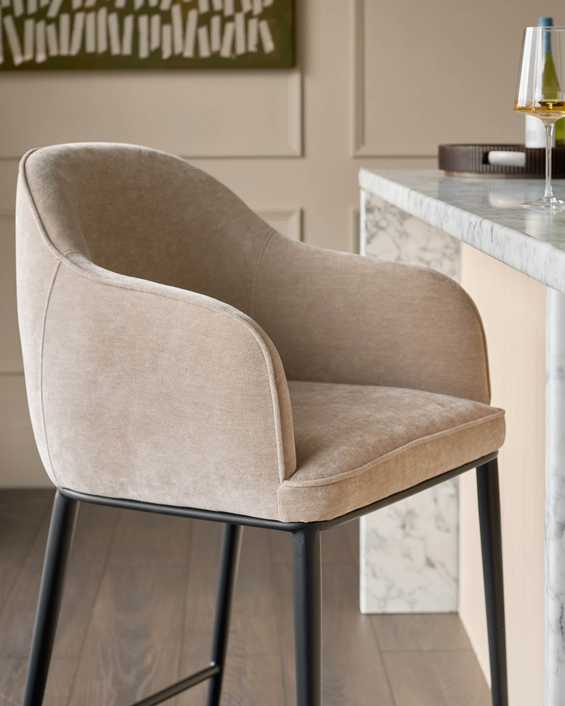 Harley bar stool in champagne fabric with curved backrest and black metal legs, positioned at marble counter.