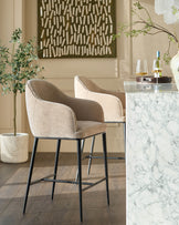 Harley bar stool in champagne fabric with black metal legs, shown in a styled interior setting.