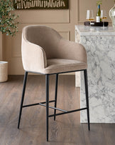Harley bar stool in champagne fabric with black metal legs, shown in a modern dining setting next to a marble counter.