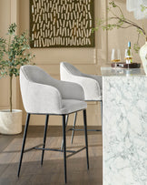 Harley bar stool in natural grey fabric with black metal legs, shown at marble counter in modern dining setting.