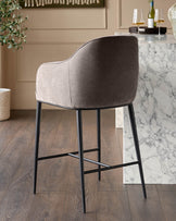 Harley bar stool in mocha fabric with curved backrest and black metal legs, shown from rear angle at marble counter.
