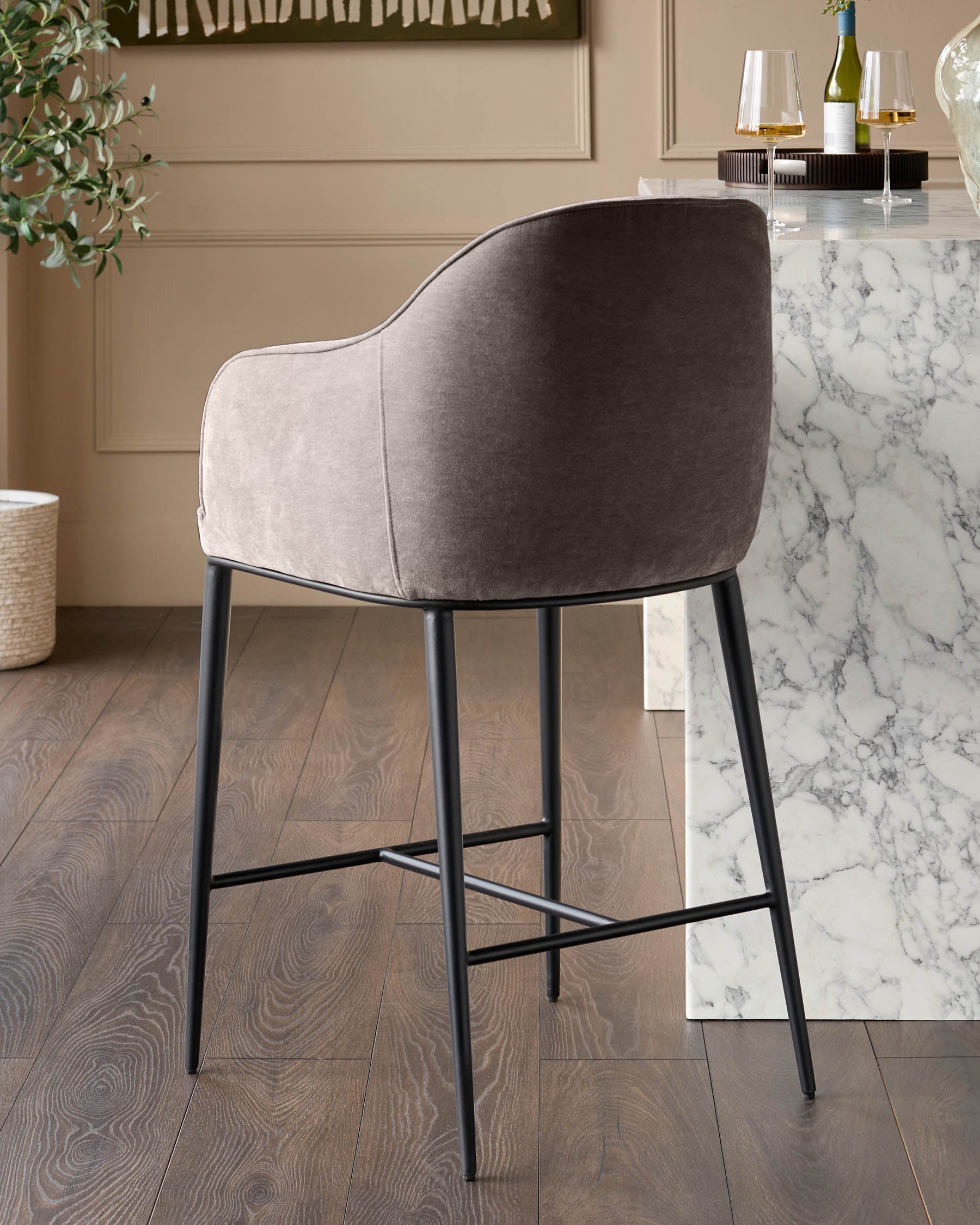 Harley bar stool in mocha fabric with curved backrest and black metal legs, shown from rear angle at marble counter.