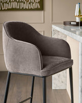 Mocha fabric bar stool with curved backrest and black metal legs, shown in side angle at a marble countertop.