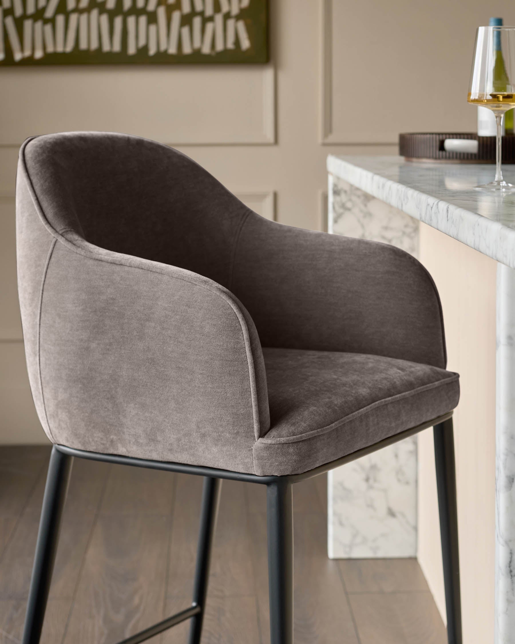 Mocha fabric bar stool with curved backrest and black metal legs, shown in side angle at a marble countertop.
